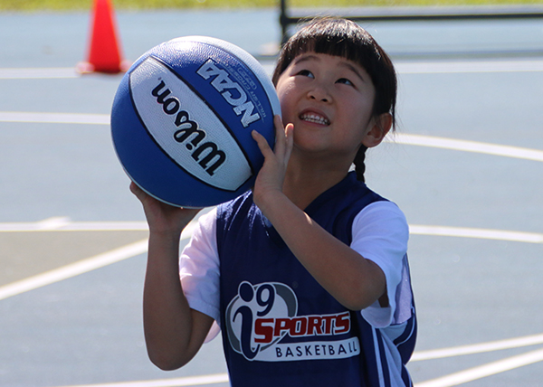 Smiling little girl in i9 Sports jersey prepares to shoot the basketball