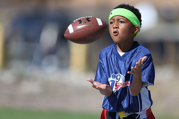 Youth Flag football player catches the football while wearing a blue i9 Sports jersey