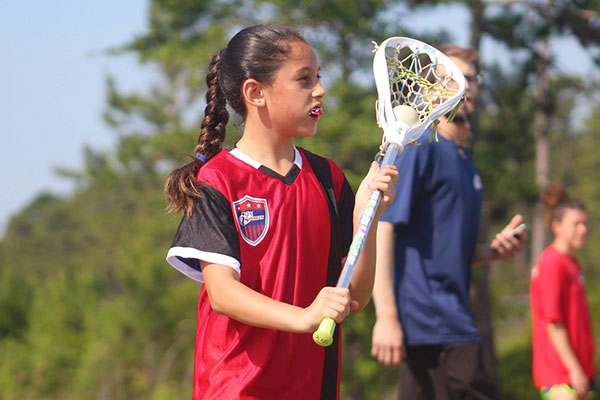 Girl in red i9 Sports jersey hods her stick and prepares to shoot the lacrosse ball