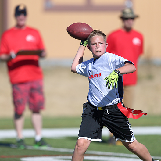 A quarterback prepares to throw the ball during a flag football game as i9 Sports coaches watch from sideline
