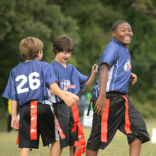 three youth flag football players laugh during a game