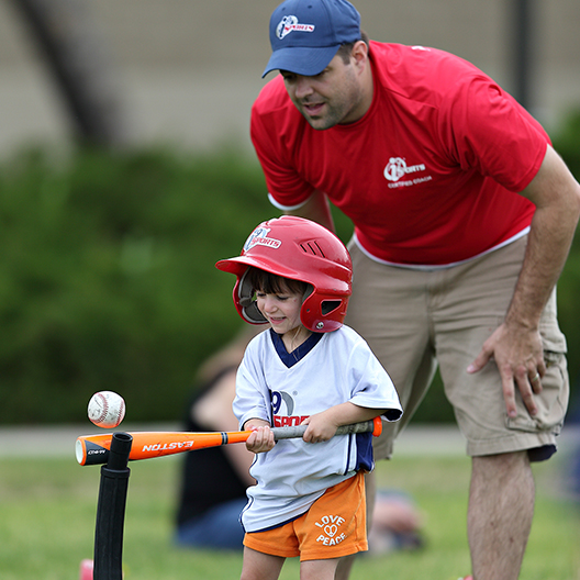 youth t ball player prepares to hit the baseball from the tee as the coach looks on