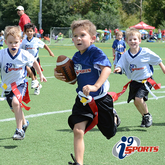 youth flag football player runs with the ball while the several defenders attempt to pull his flag