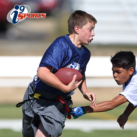 Kid runs with football during a flag football game as a defender prepares to pull his flag.