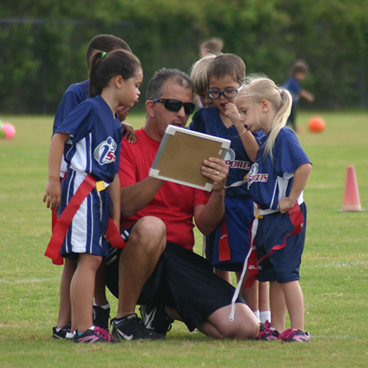 flag football coach reviews plays in the huddle while players look on