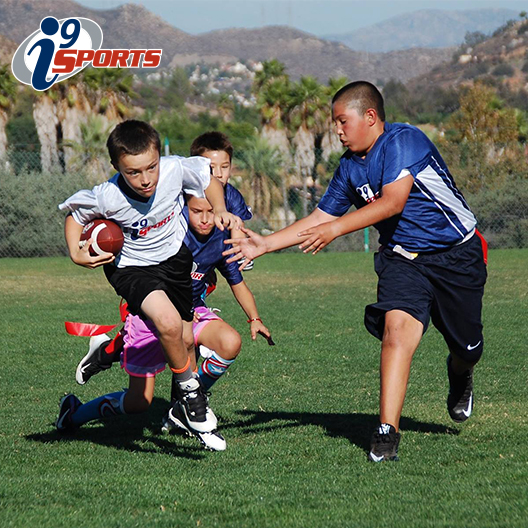 A San Diego youth flag football player runs with the ball while another attempts to pull his flag belt