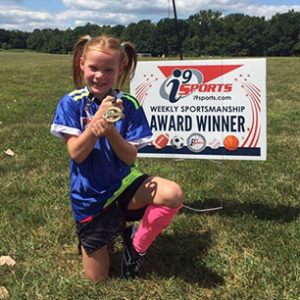 Female Soccer player poses with i9 Sports sportsmanship medal and sign after winning the weekly award