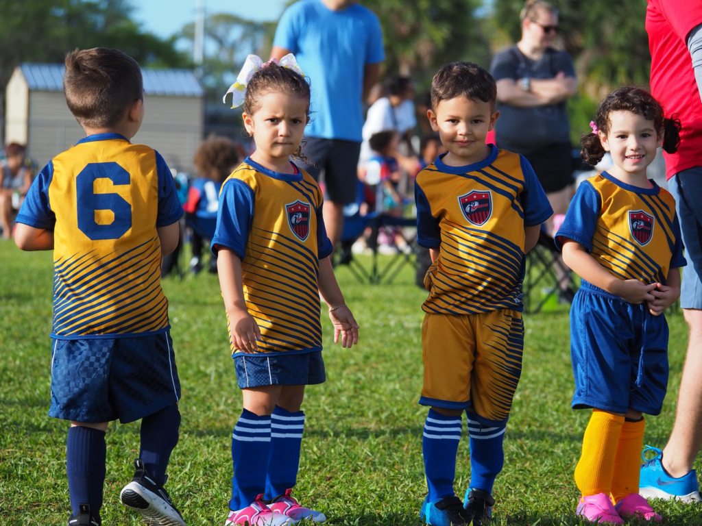 Four children lined up ready for soccer practice in their yellow and blue jerseys.
