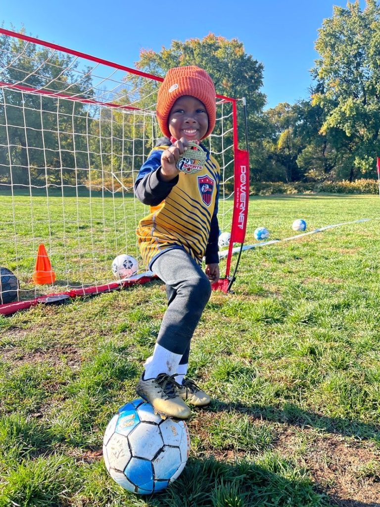 Child youth soccer player with winter hat on and his foot on top of soccer ball.