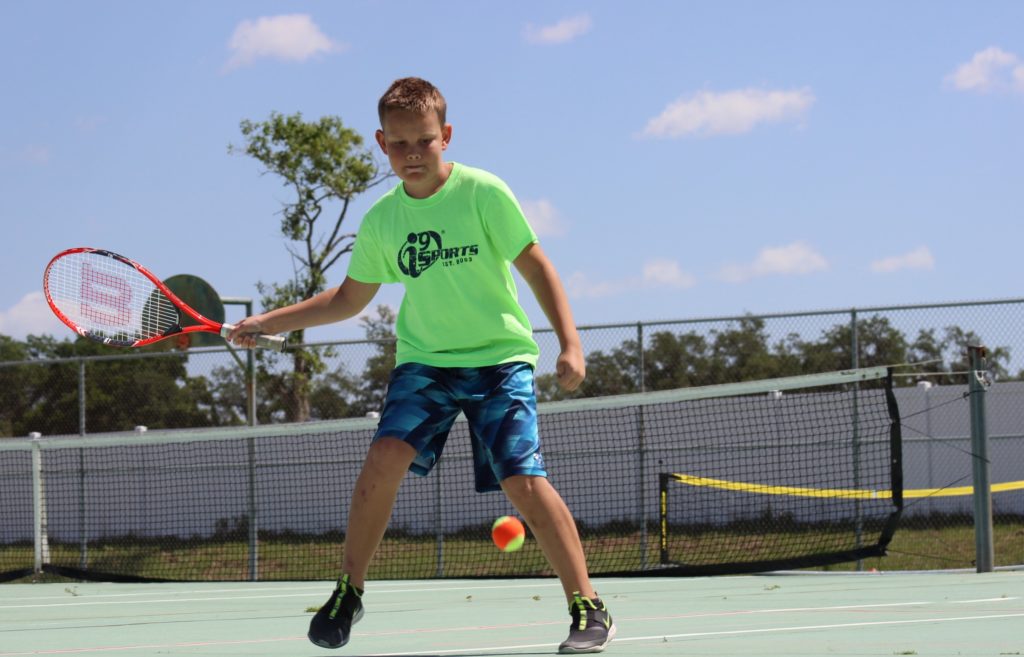 Young boy swinging a tennis racket at a tennis ball.