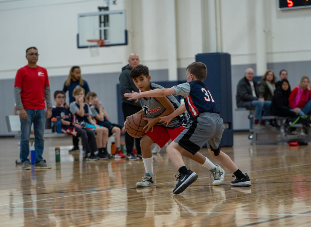 Two pre-teen boys playing youth basketball inside of a gym.