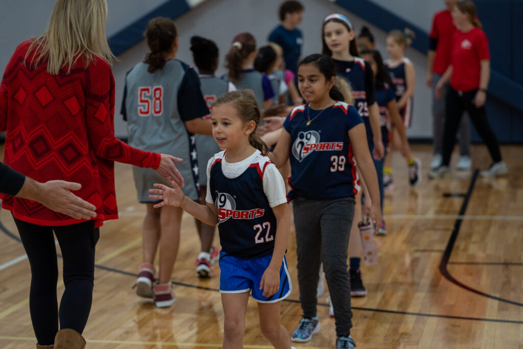 Young female basketball players lined up and high fiving each other after the game.