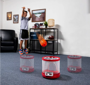 A pre-teen boy shooting a foam basketball into a moving target on the floor. the target looks like a red Roomba with a white basketball net on top.