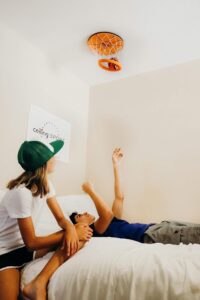 Two young teens playing with the Ceiling Swish which is an upside down basketball hoop net attached to the ceiling. You can throw the plush basketball into the net on the ceiling to pass the time.