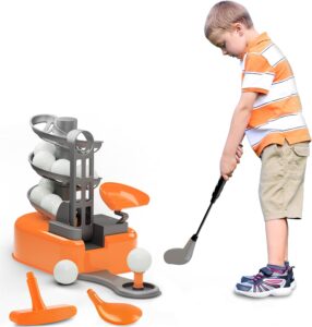 A young boy in an orange and white striped shirt and khaki shorts, and Velcro sneakers holding a plastic golf club while the toy loads a plastic golf ball onto a tee for him to hit.