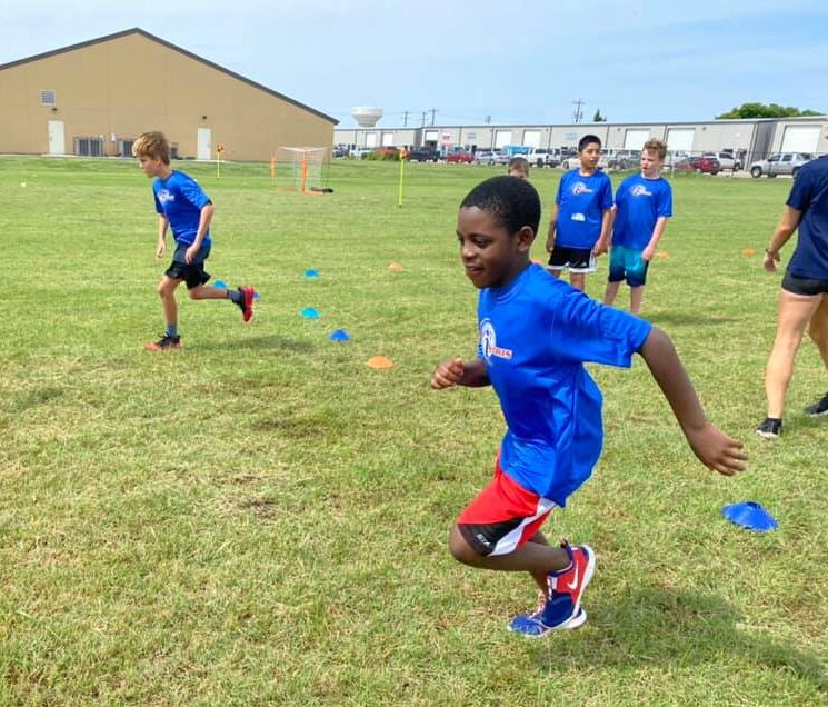 Two pre-teen boys in royal blue i9 Sports t-shirts running from blue cones during an i9 Sports camp or clinic.