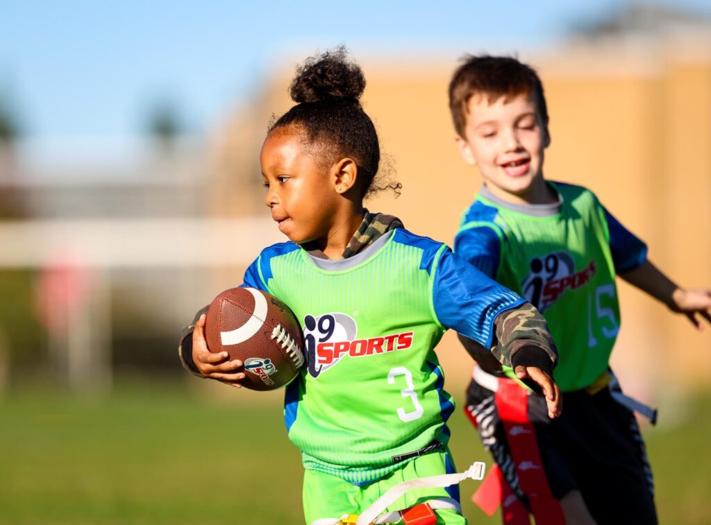 Young girl running with a football during an i9 Sports flag football game.