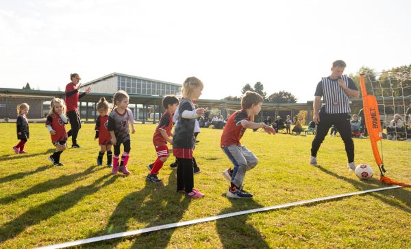 Seven young girls and boys playing soccer and watching the soccer ball as it is inches form going into the goal. The ref is standing by to blow the whistle. We have no idea if the ball went in after this photo, the suspense is killing us too!