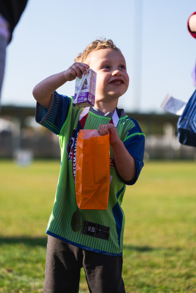 Young athlete holding an orange paper bag and a juice box with a big smile on his face.