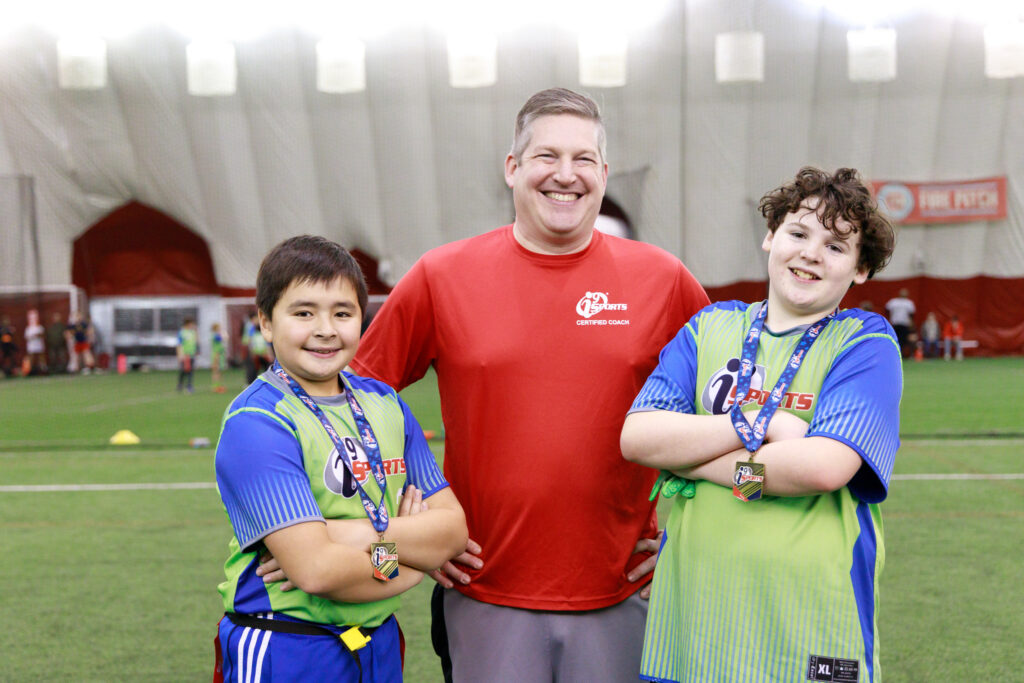 An i9 Sports flag football coach and two of the flag football players wearing their sportsmanship medals and smiling for the camera.