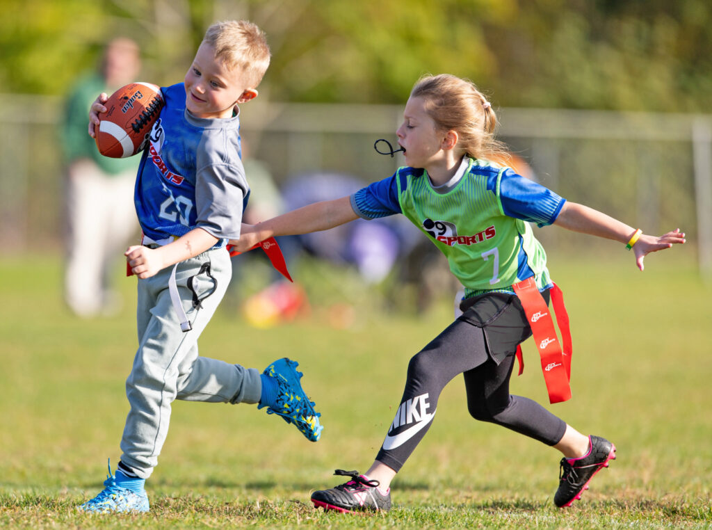 A young girl chasing down her opponent in a co-ed flag football game and grabbing his flags.