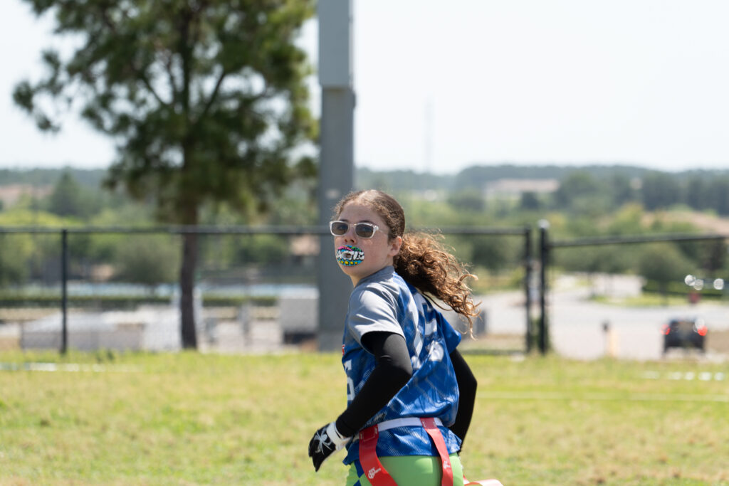 Teen girl running her wide receiver route ready to catch the touchdown during her girls' flag football game.