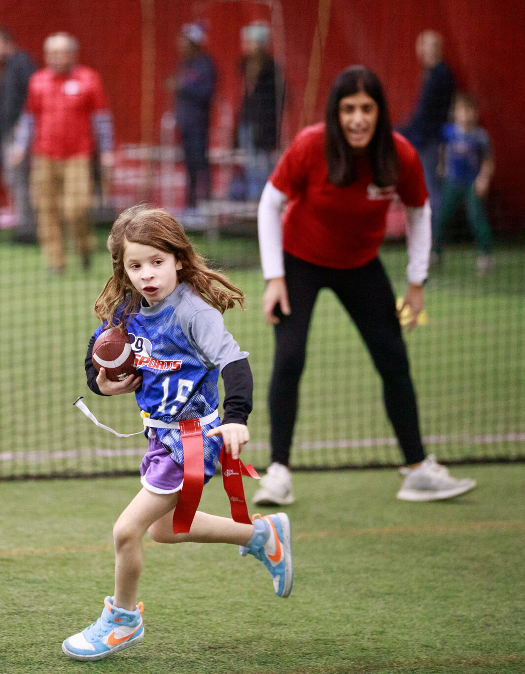 A female flag football coach cheering on her female flag football player as she runs towards the endzone with the ball.
