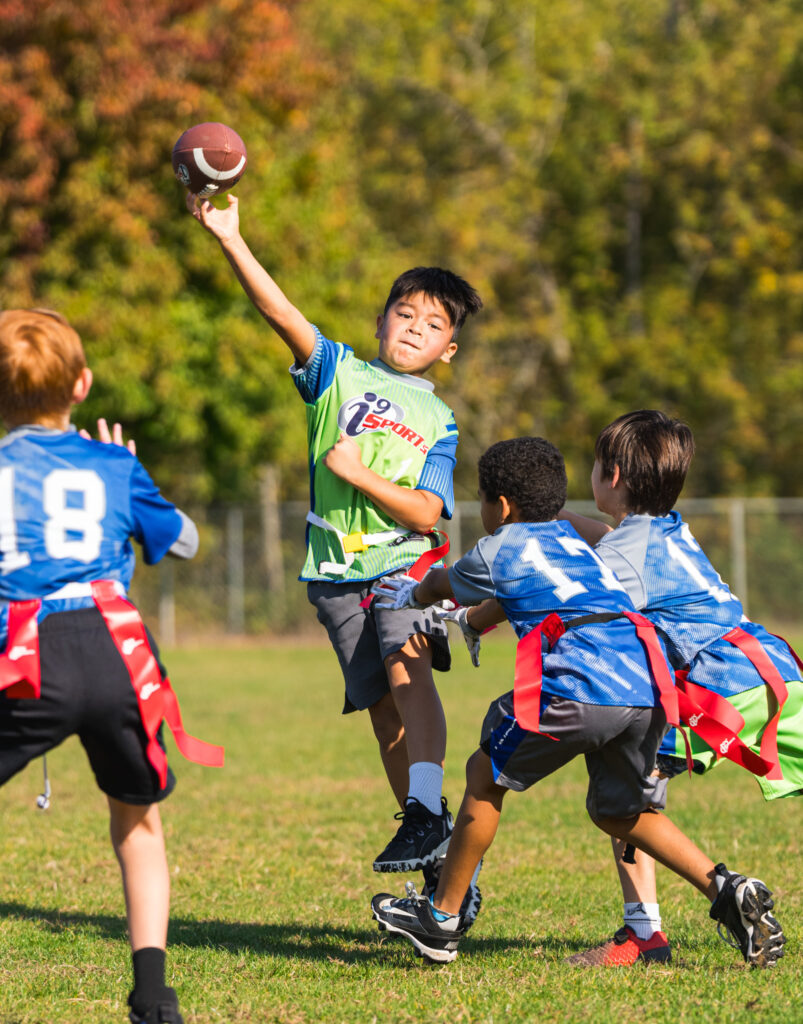 Young boy playing quarterback during his youth flag football game. He's in the pocket, throwing the ball. As the ball is leaving his hands, the defenders are grabbing for his flags, but not soon enough!