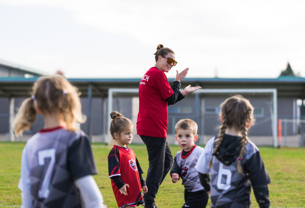 A female i9 Sports coach clapping and motivating her peewee soccer team.
