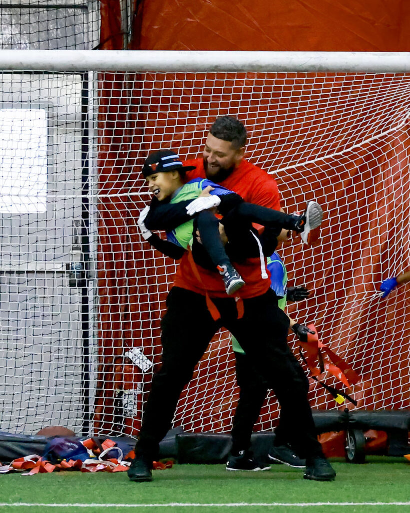 Parent-coach lifting his child after an exciting play in their indoor flag football game.