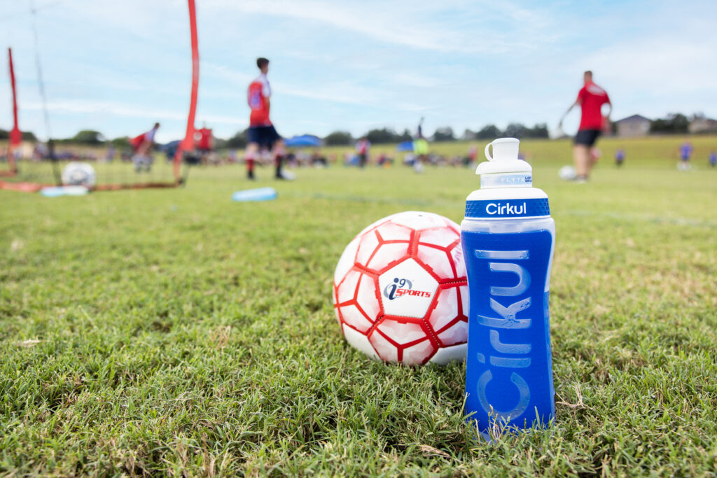 An i9 Sports soccer ball next to a bright royal blue and transparent Cirkul water bottle announcing the partnership between i9 Sports and Cirkul.