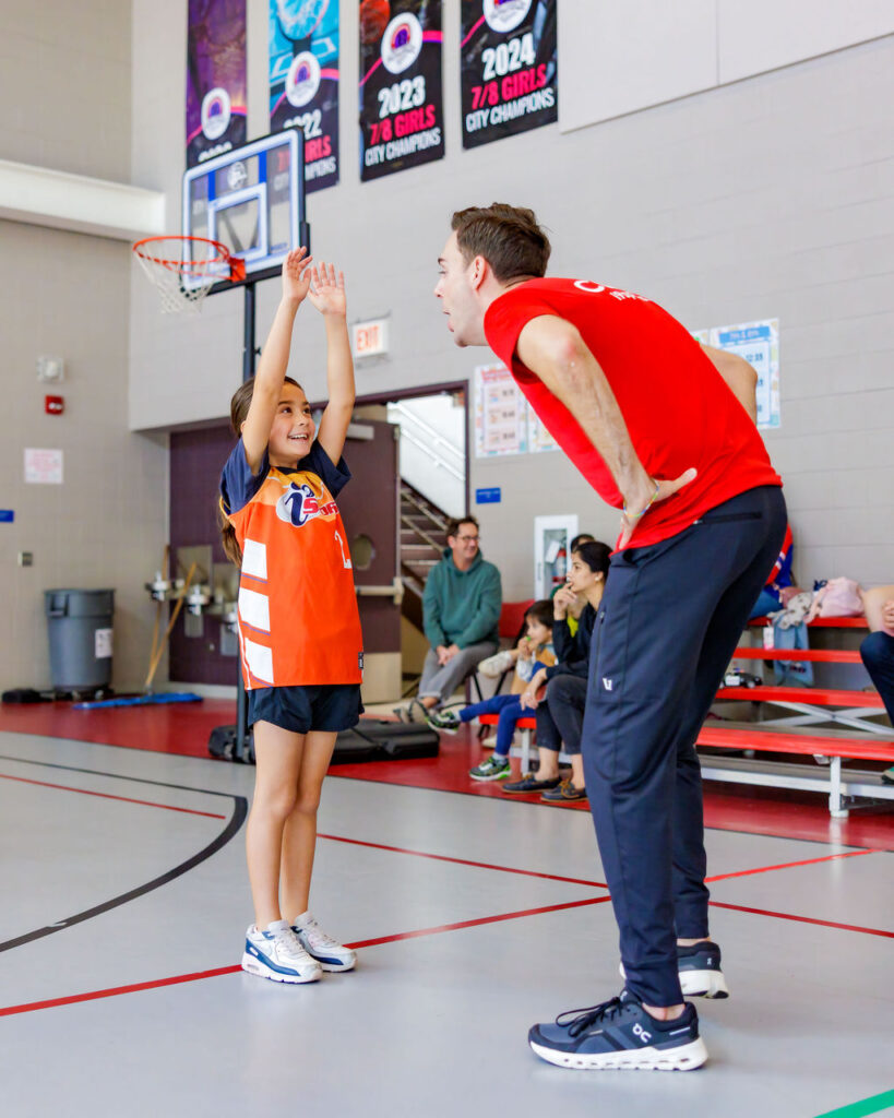 Basketball coach teaching a young girl how to keep her hands up on defense while making her laugh.